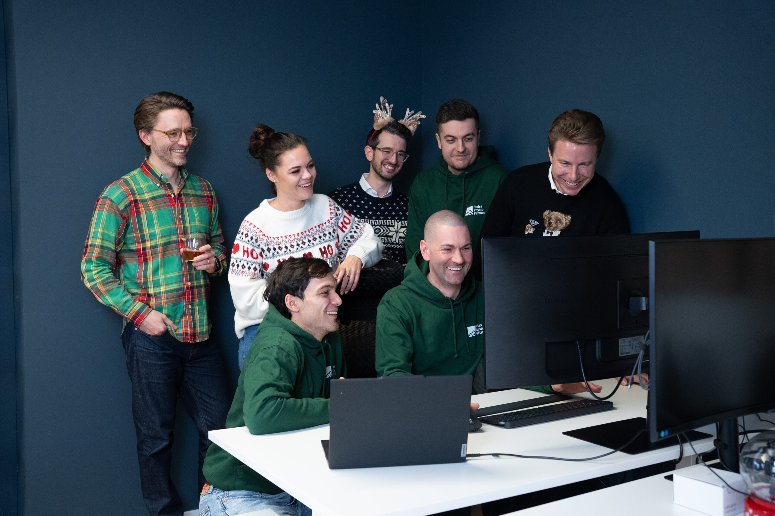 Das team von Swiss Physio partner sitz in weihnachtlicher Kleidung gemeinsam vor dem Computer